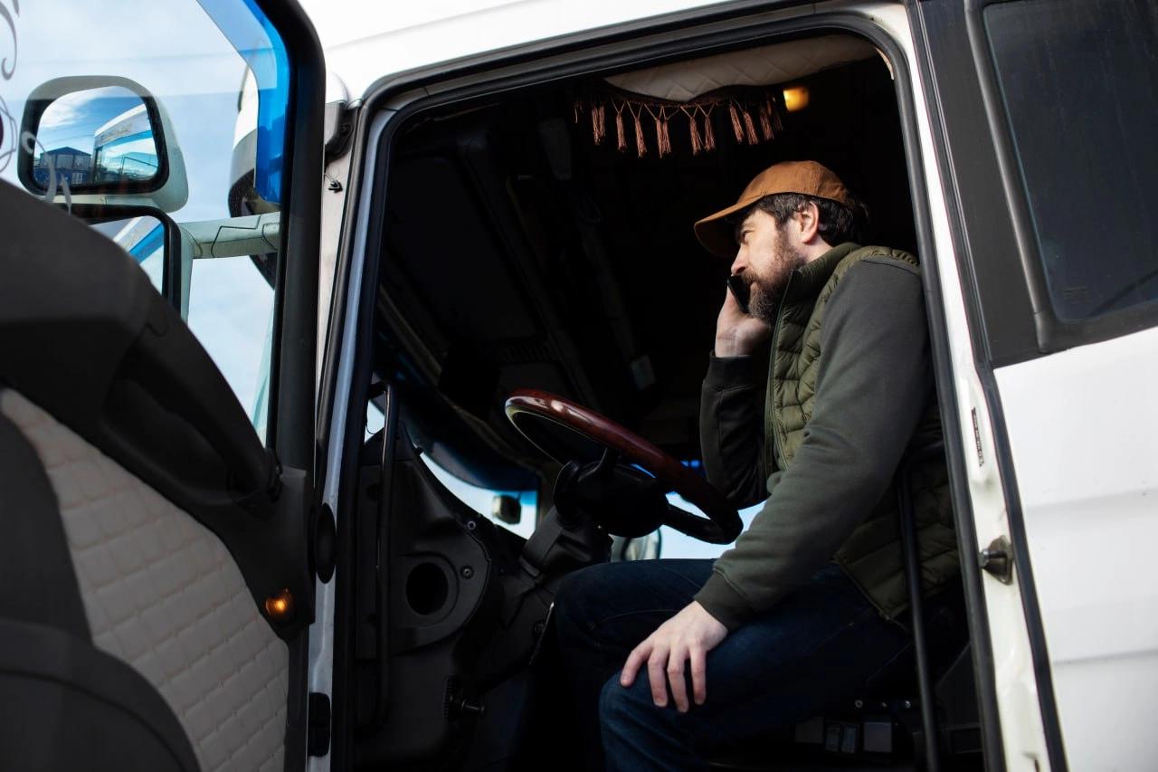 Truck driver communicating by phone inside cab representing responsive and reliable shipping services near me for local freight coordination
